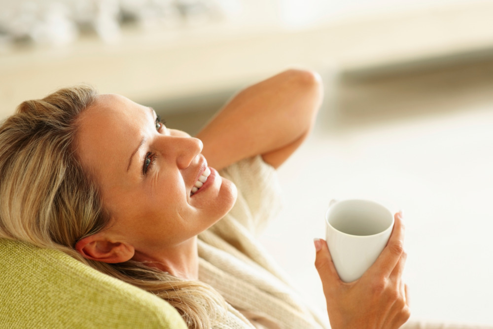 Woman happily relaxing in a chair while holding a cup of tea.