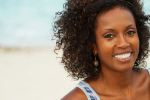 Close up of a woman's face smiling with a beach background.