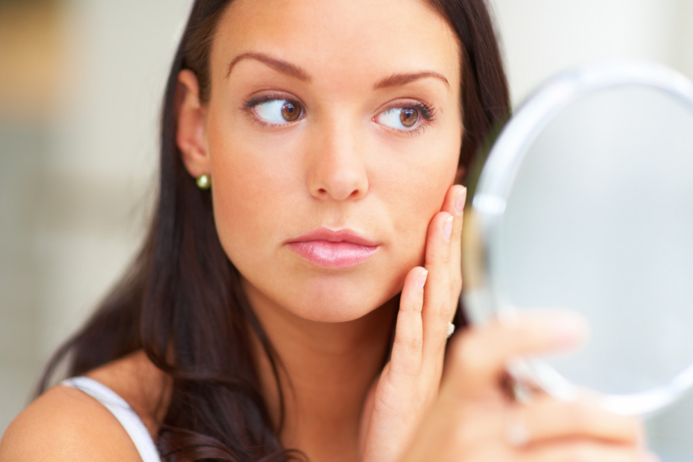 Woman examining at her face in a small makeup vanity mirror.