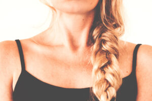 A close up of a woman's neckline. She's wearing a black tank top and has braided hair.