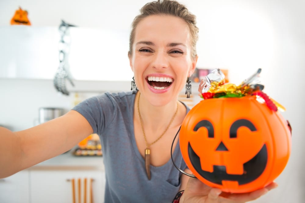 Happy woman taking a selfie with halloween bucket full of candy.